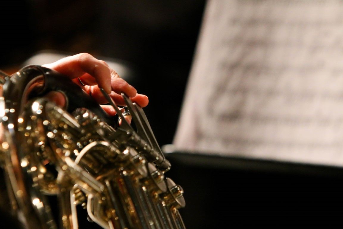 A horn player's hand resting in the bell of the instrument, sheet music soft in the background