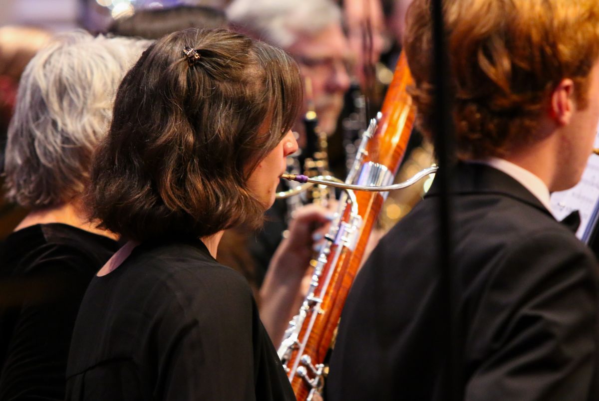 A bassoonist mid-phrase in warm stage light, the clarinet row soft behind her