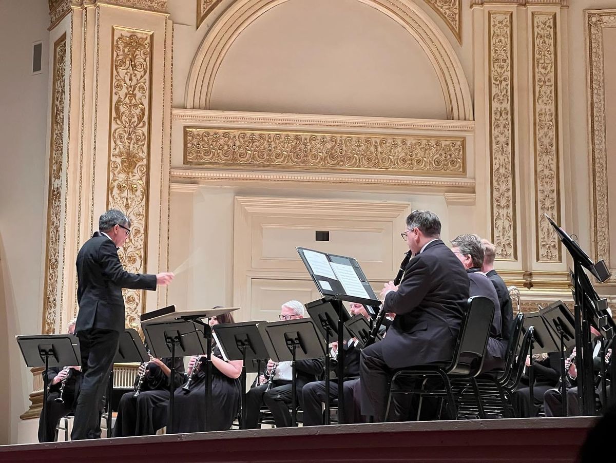A conductor leading the Clarinet Choir beneath Carnegie Hall's gilded walls